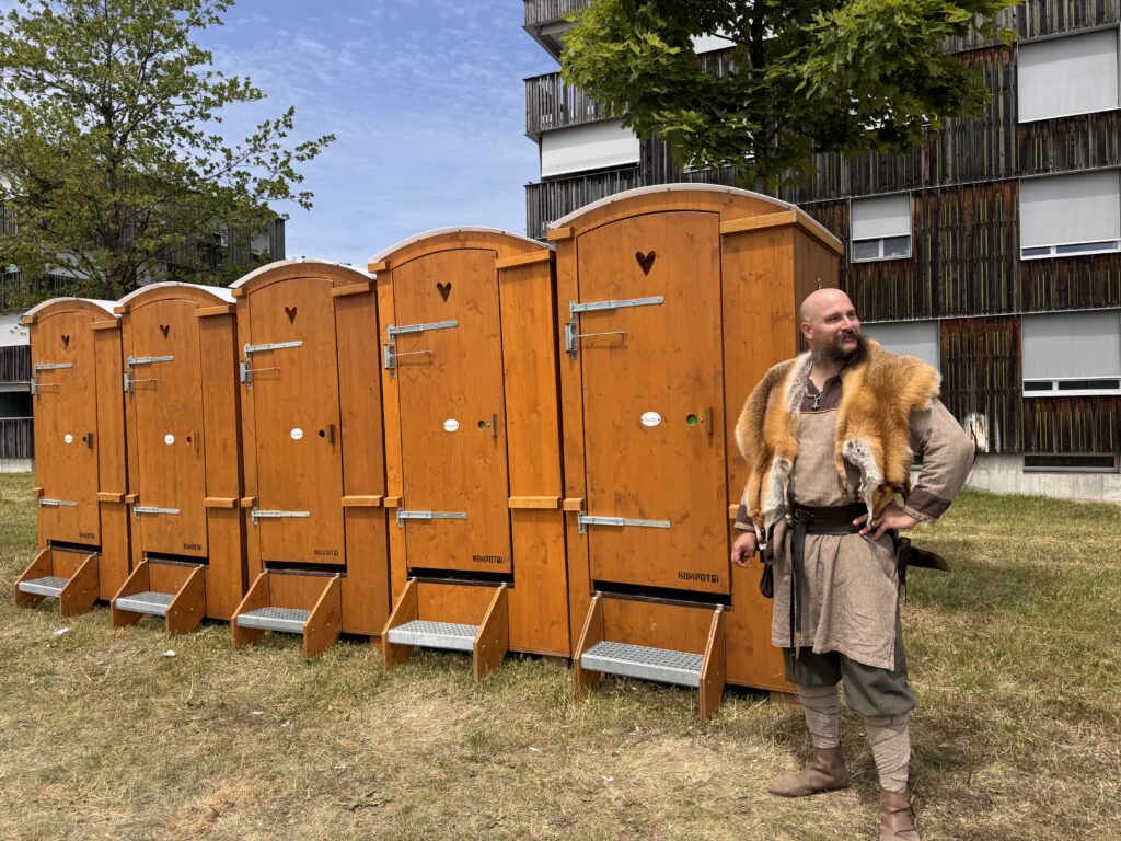 Mann in Mittelalter-Kleidung vor Kompotoi Komposttoiletten / Kompotoi Classic